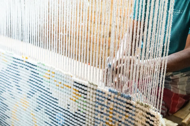 A rug being hand-woven on a loom, showing warp and weft threads